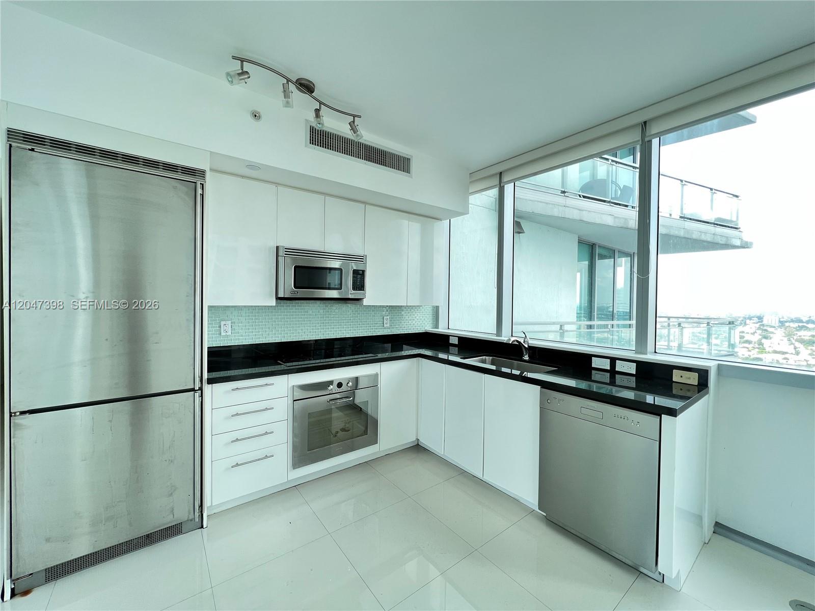 A modern kitchen features white cabinets, black countertops, stainless steel appliances, and floor-to-ceiling windows — 92 SW 3rd St # 3310, Miami FL 33130, MIAMI, FL