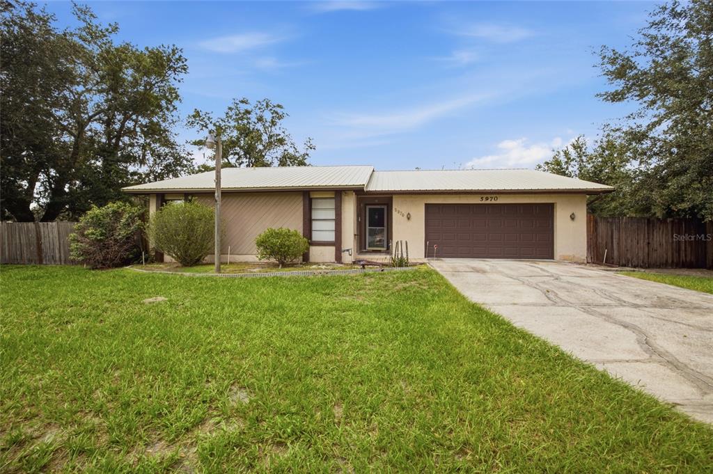 A single-story house with a metal roof, brown garage door, and a concrete driveway — 5970 SOUTHWIND DRIVE, MULBERRY, FL
