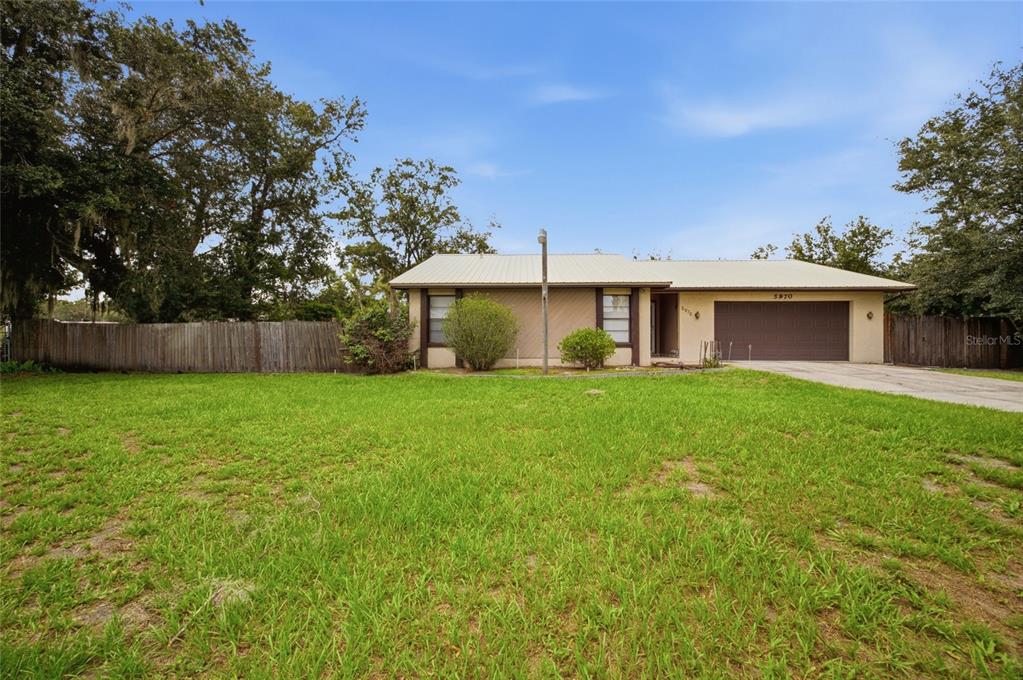 A single-story house with a metal roof, brown garage door, and a large front lawn — 5970 SOUTHWIND DRIVE, MULBERRY, FL