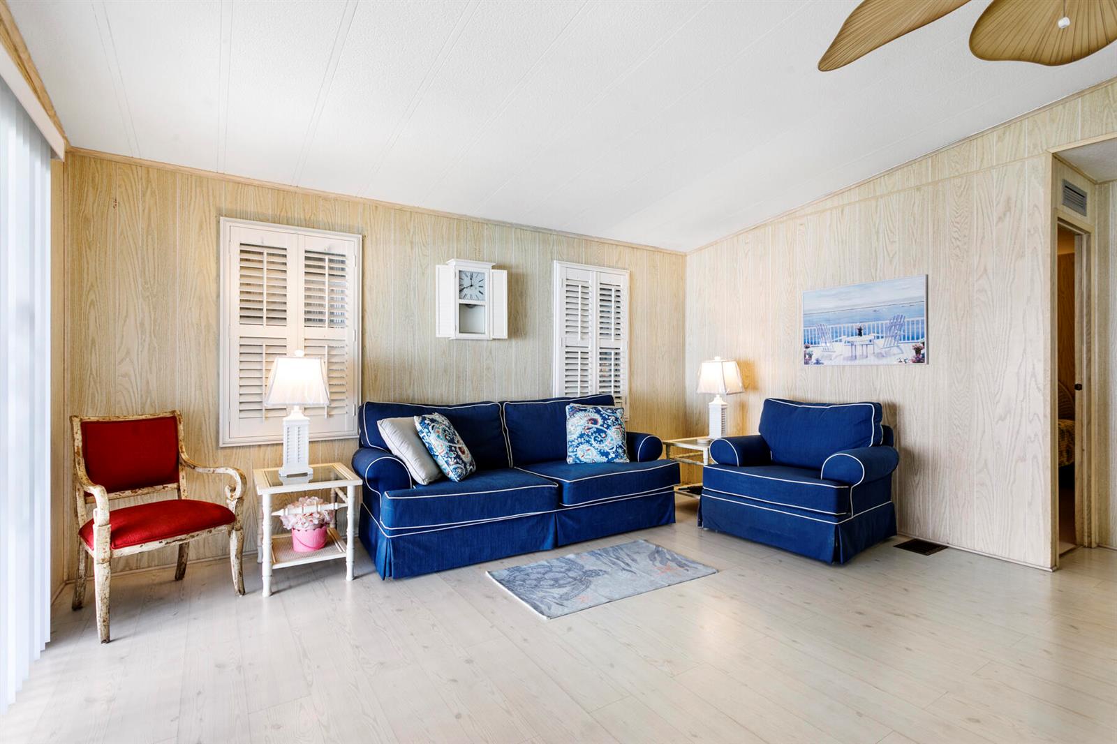 A living room features wood-paneled walls, a blue sofa and armchair, and a red chair — 18007 Huapi Bay, Boynton Beach FL 33436, BOYNTON BEACH, FL