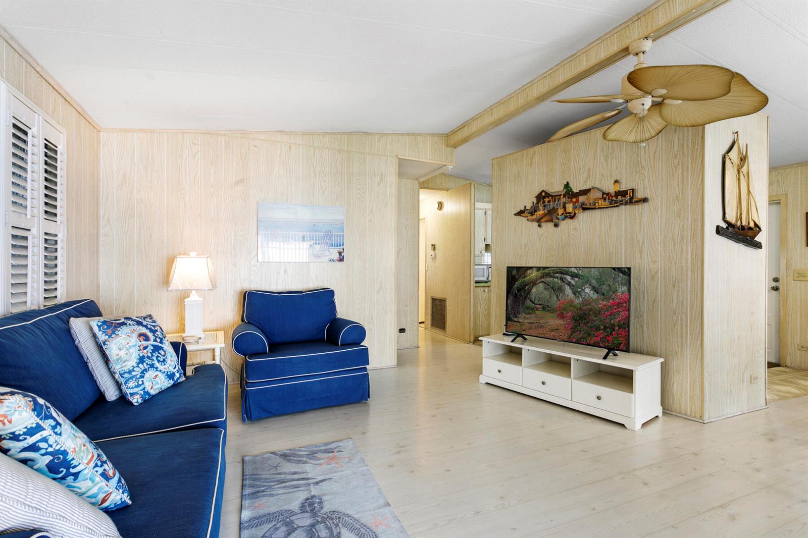 A living room features wood-paneled walls, a blue sofa and armchair, and a ceiling fan — 18007 Huapi Bay, Boynton Beach FL 33436, BOYNTON BEACH, FL