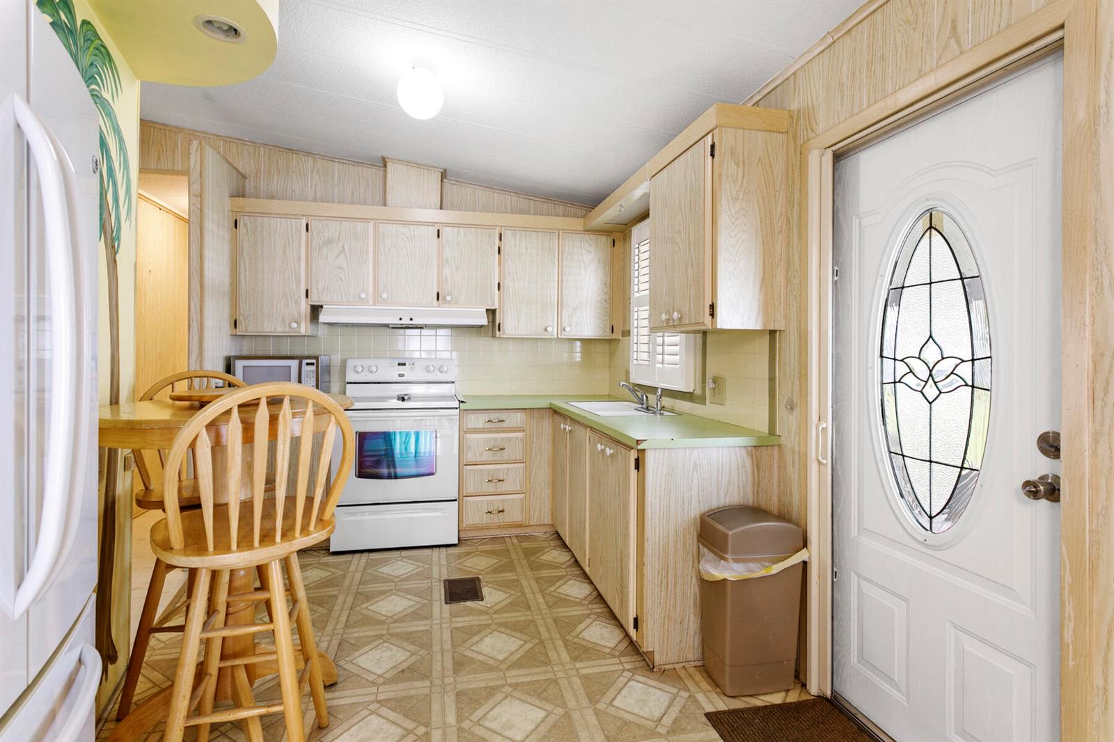 A kitchen features wood-paneled cabinets, light green countertops, a white stove, and patterned flooring — 18007 Huapi Bay, Boynton Beach FL 33436, BOYNTON BEACH, FL