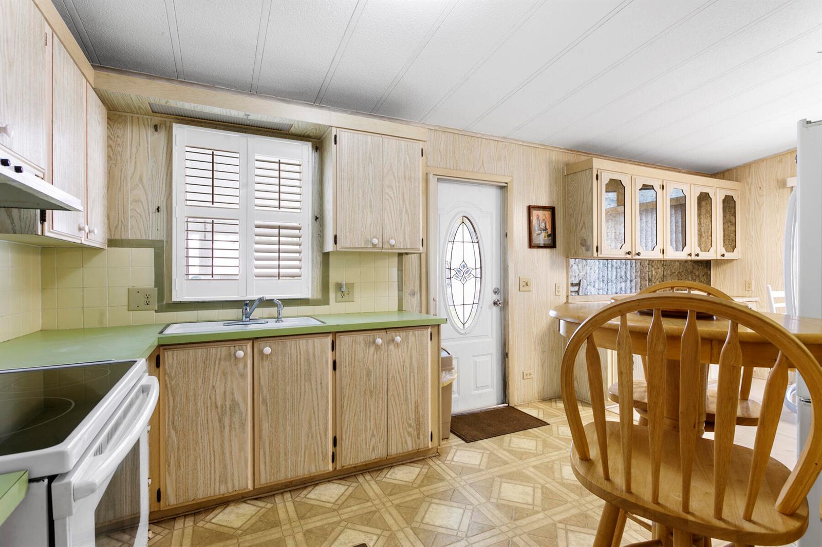A kitchen with wood-paneled walls, light wood cabinets, green countertops, and a dining area — 18007 Huapi Bay, Boynton Beach FL 33436, BOYNTON BEACH, FL