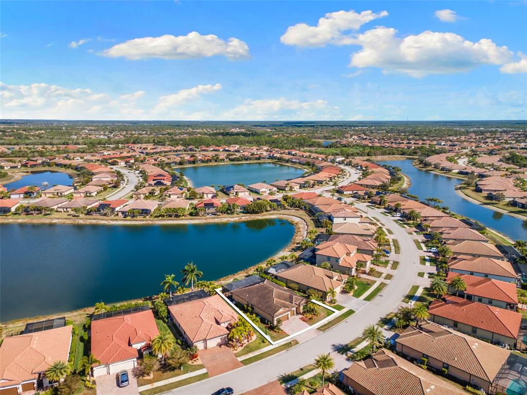 An aerial view shows a suburban neighborhood with houses surrounding a large lake — 13238 FAMIGLIA DRIVE, VENICE, FL