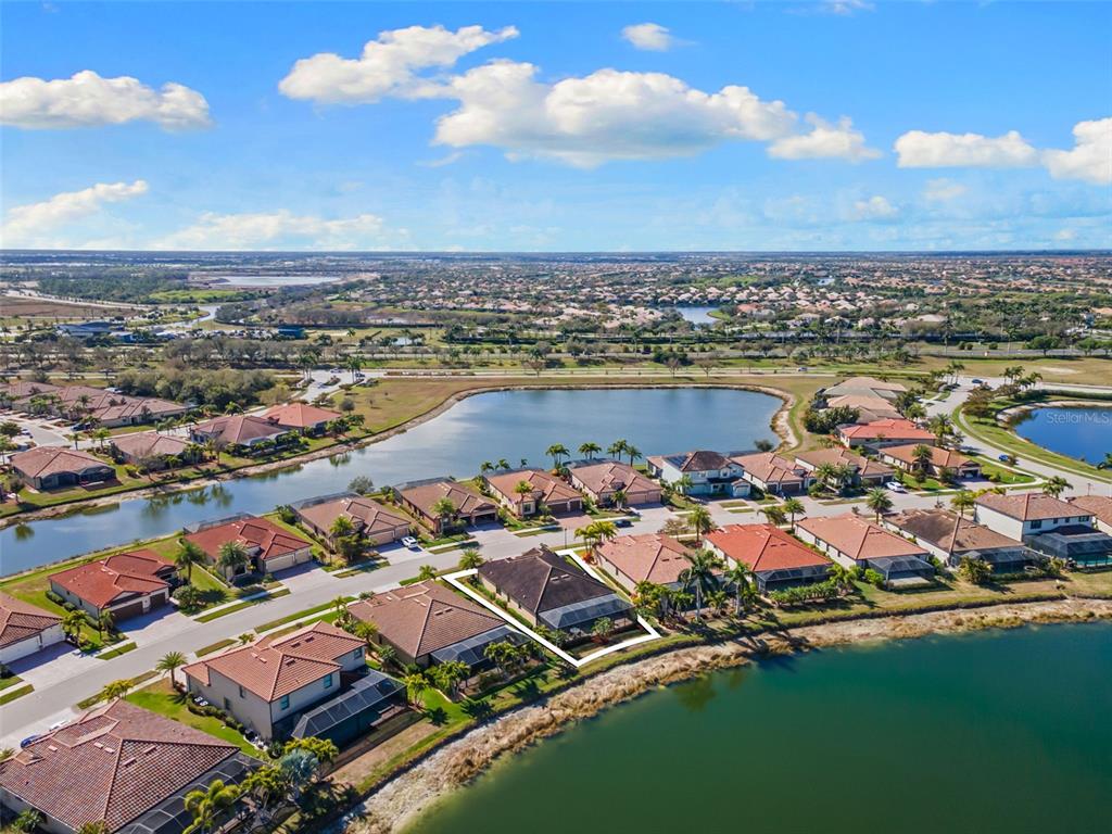 An aerial view shows a residential house with a screened pool deck beside a lake — 13238 FAMIGLIA DRIVE, VENICE, FL