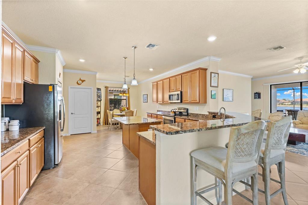 A kitchen with light wood cabinets, granite countertops, a center island, and tile flooring — 13238 FAMIGLIA DRIVE, VENICE, FL
