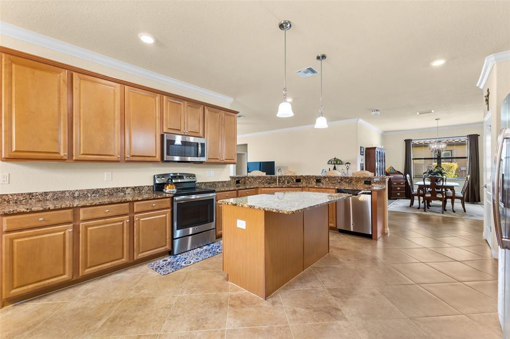 A kitchen with wood cabinets, granite countertops, a center island, and tile flooring — 13238 FAMIGLIA DRIVE, VENICE, FL