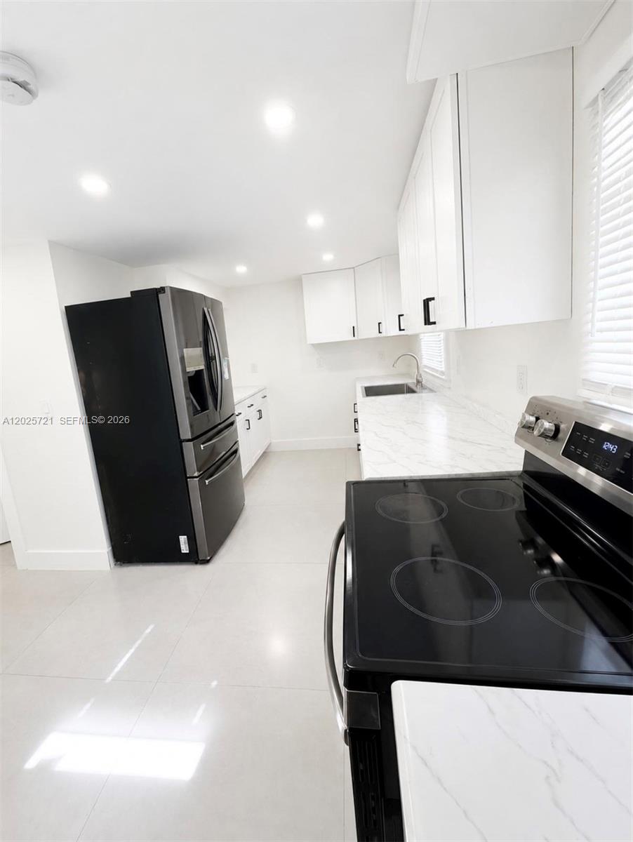 A modern kitchen features white cabinets, marble-look countertops, and black stainless steel appliances — 4125 N 32nd Ct, Hollywood FL 33021, HOLLYWOOD, FL