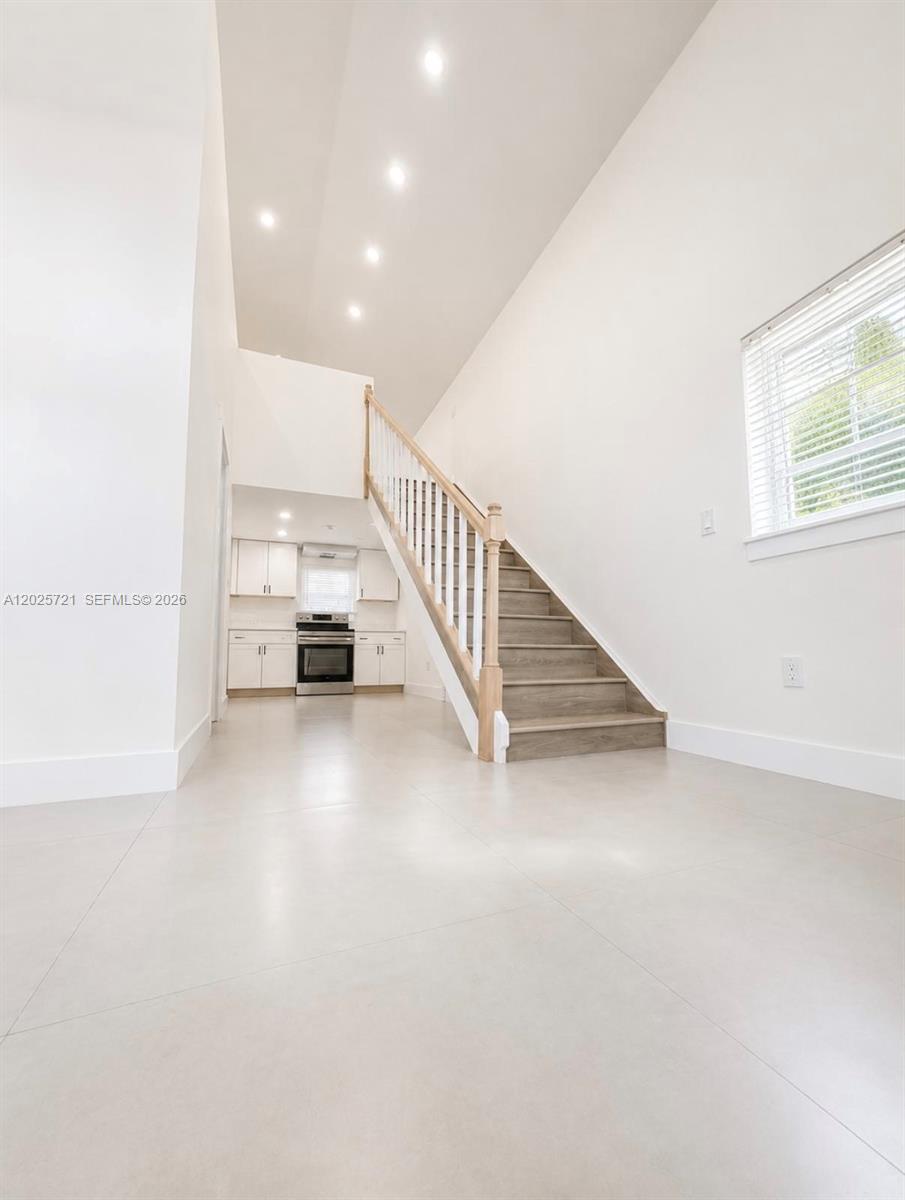 A bright, minimalist room features white walls, tile flooring, and a staircase leading upstairs — 4125 N 32nd Ct, Hollywood FL 33021, HOLLYWOOD, FL