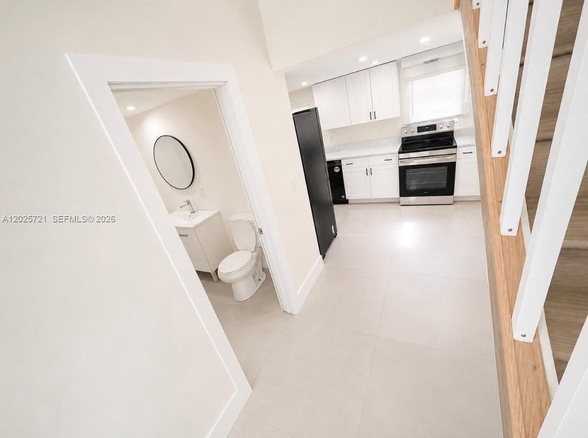 A small bathroom sits beside a kitchen featuring white cabinets and stainless steel appliances — 4125 N 32nd Ct, Hollywood FL 33021, HOLLYWOOD, FL