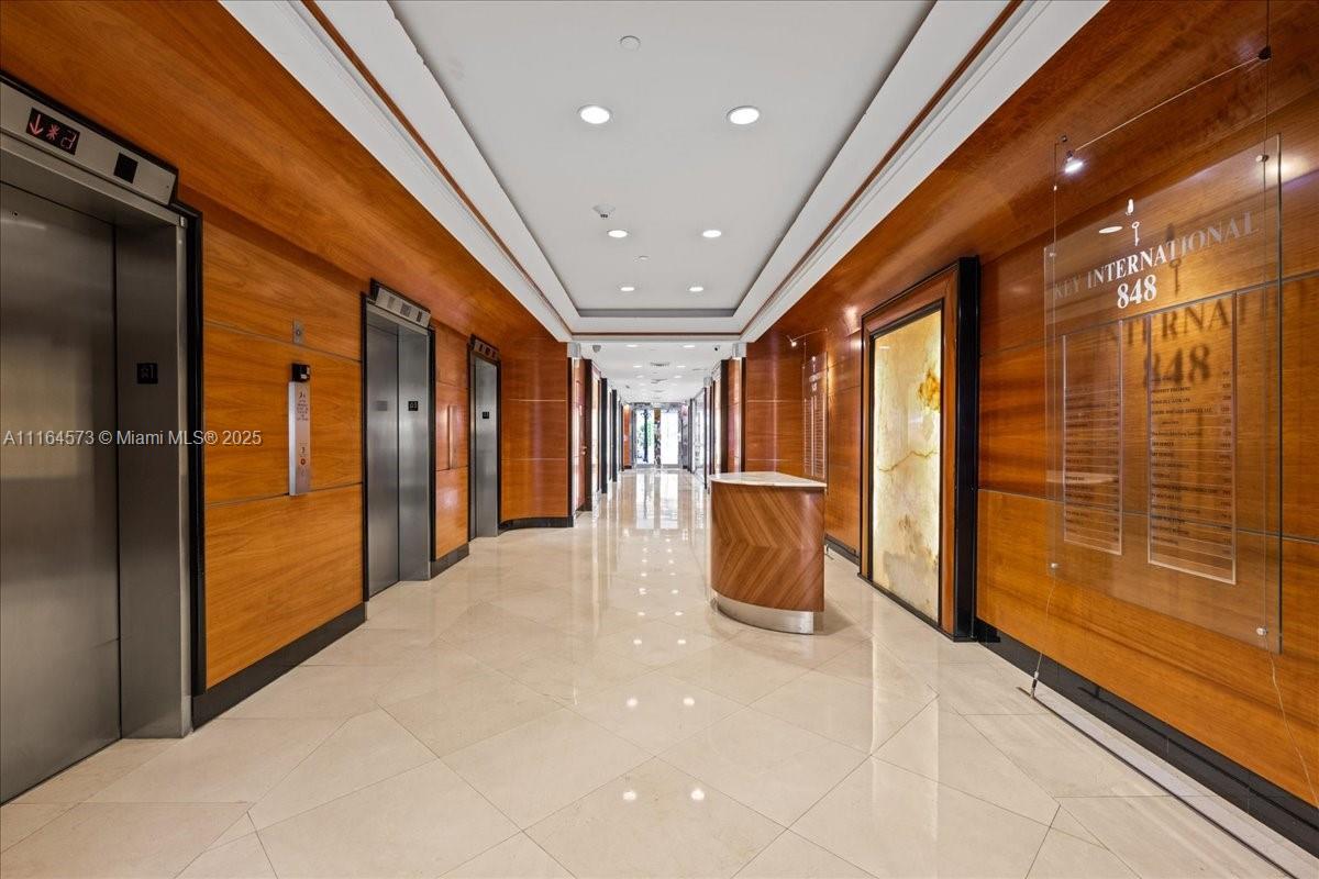 A modern office building hallway features wood-paneled walls, elevators, and a polished tile floor — 848 Brickell Ave, Miami FL 33131, MIAMI, FL