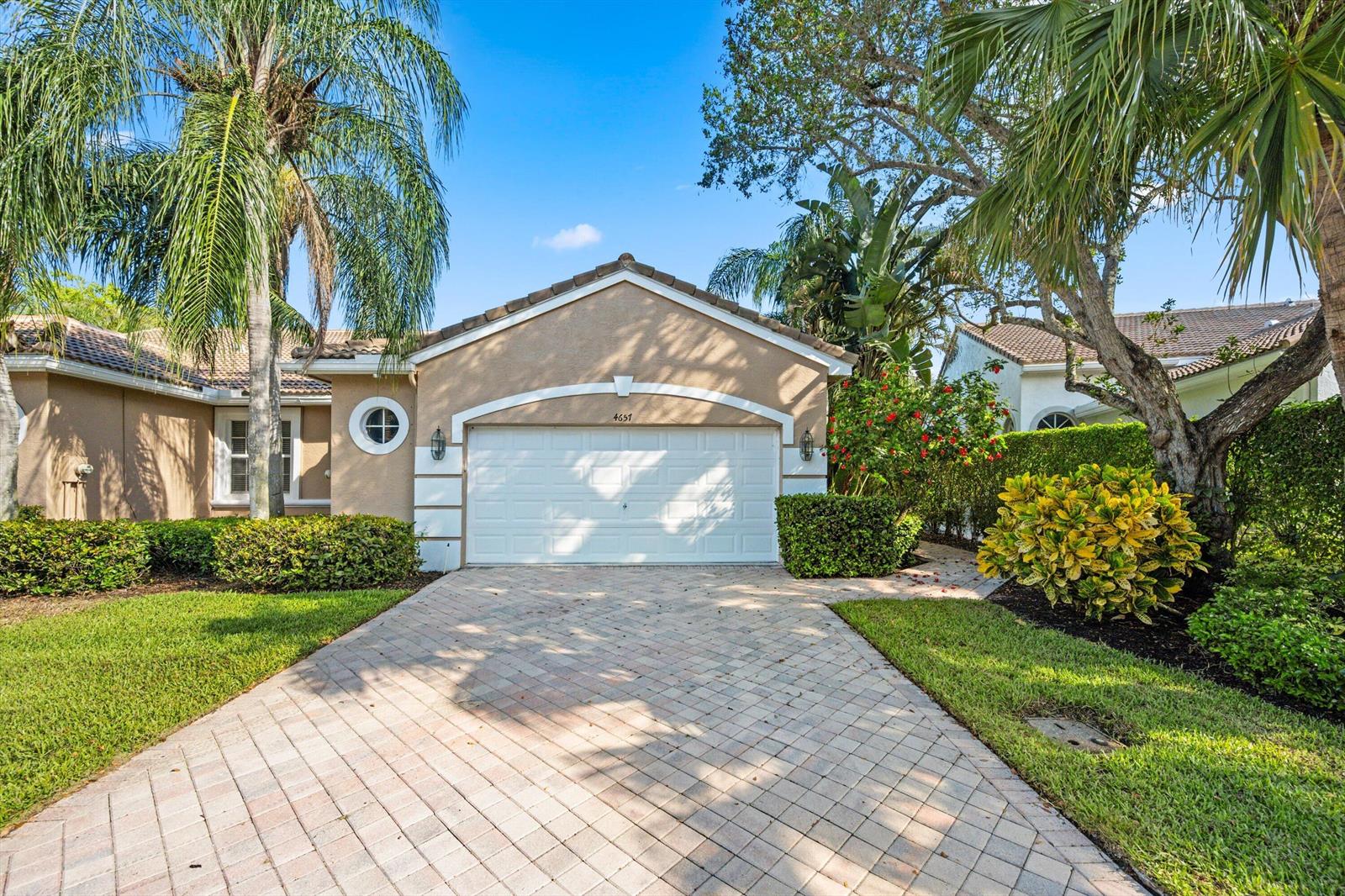 A beige house with a white garage door and a paved driveway under a blue sky — 4657 Carlton Golf Drive, Lake Worth FL 33449, LAKE WORTH, FL