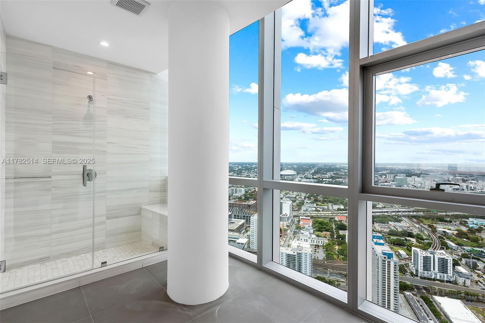 A modern bathroom features a glass-enclosed shower, a large structural pillar, and floor-to-ceiling windows — 851 NE 1st Ave # 5500, Miami FL 33132, MIAMI, FL