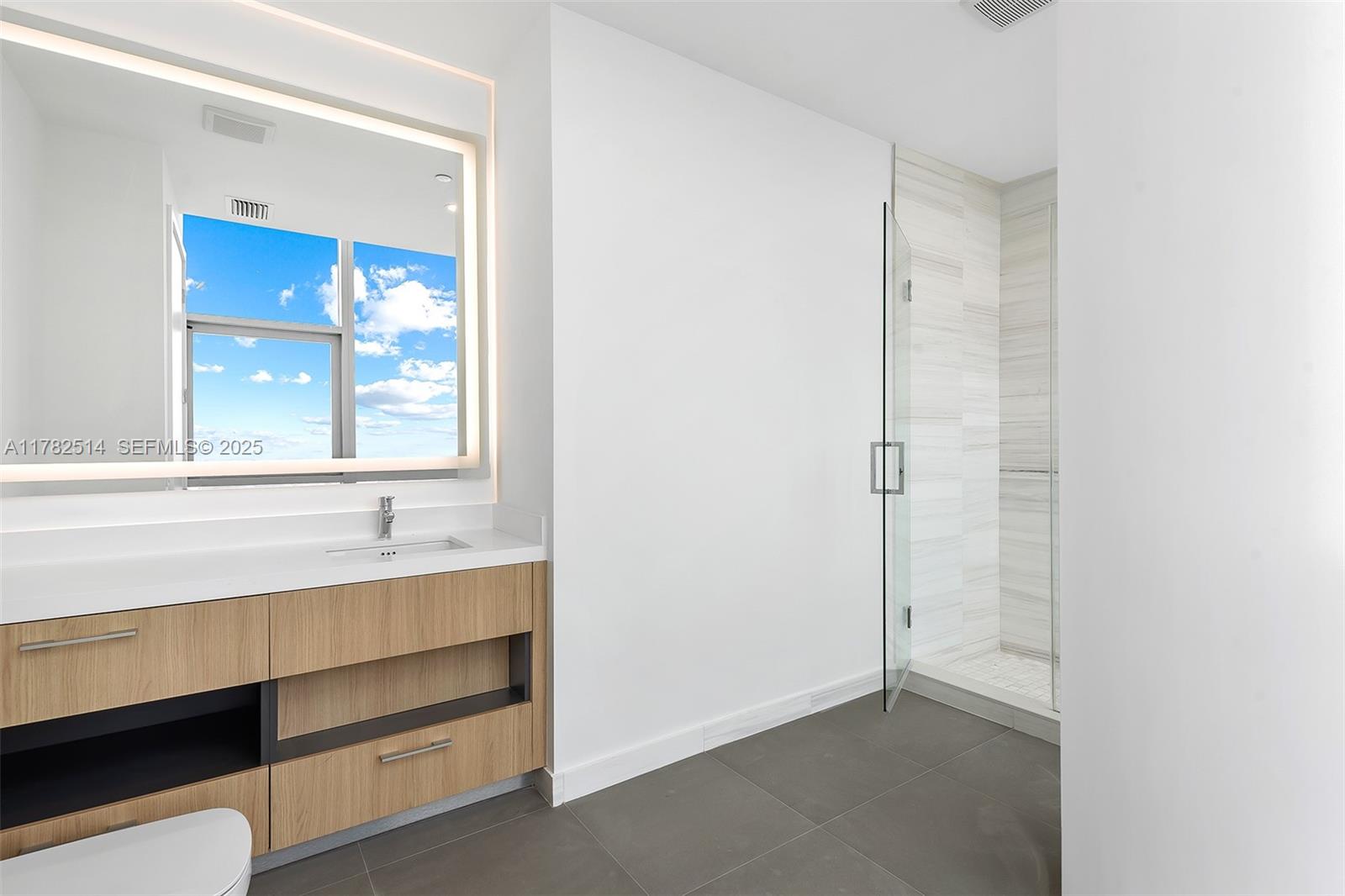 A modern bathroom features a wood vanity, a large illuminated mirror, and a glass-enclosed shower — 851 NE 1st Ave # 5500, Miami FL 33132, MIAMI, FL