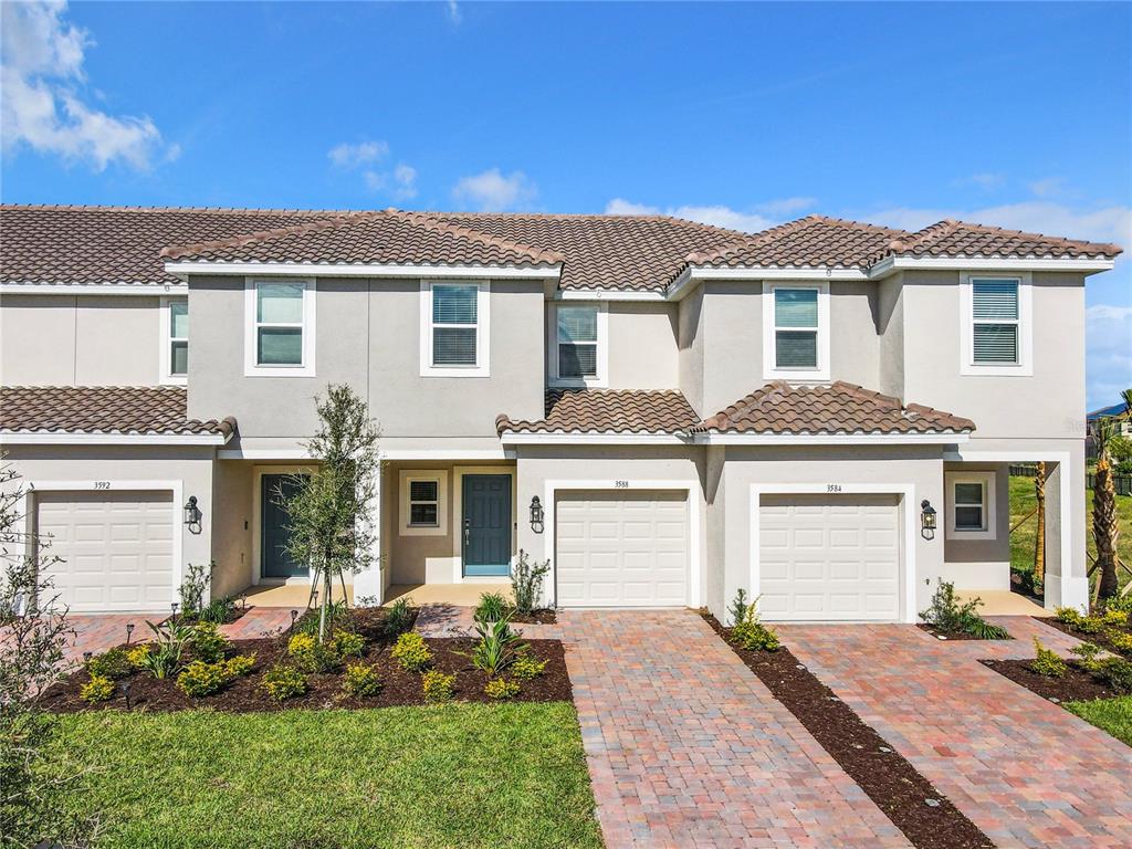 A row of three attached townhouses features beige stucco facades, tiled roofs, and brick paver driveways — 3588 LANDING NET DRIVE, KISSIMMEE, FL