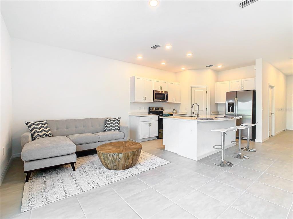 A modern open-concept kitchen and living area with white cabinetry, stainless appliances, and tile flooring — 3588 LANDING NET DRIVE, KISSIMMEE, FL