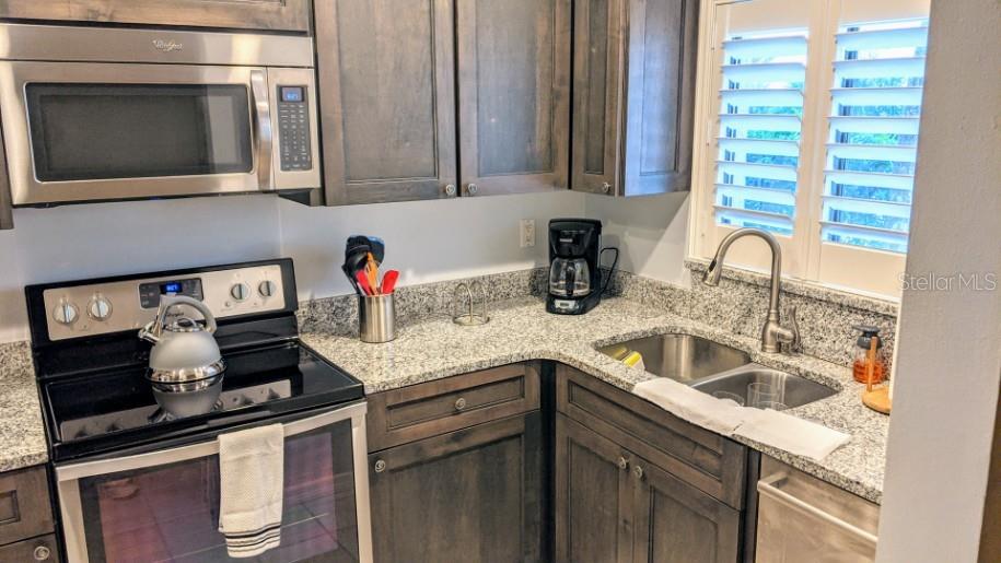 A kitchen features dark wood cabinets, granite countertops, a stainless steel microwave, and a stove — 1624 STICKNEY POINT UNIT 107, SARASOTA, FL