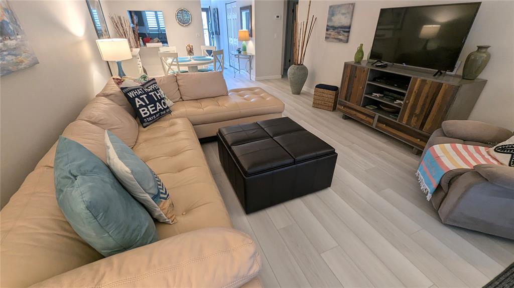A living room features a large beige sectional sofa, a black ottoman, and a television console — 1624 STICKNEY POINT UNIT 107, SARASOTA, FL