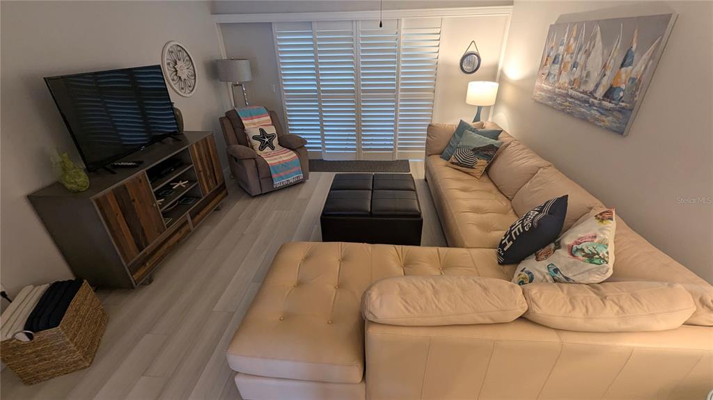 A living room features a beige sectional sofa, a television on a wooden console, and shutters — 1624 STICKNEY POINT UNIT 107, SARASOTA, FL
