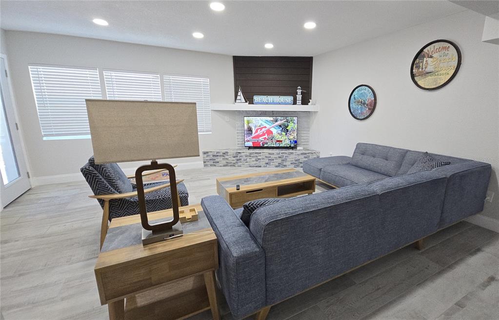 A living room features a sectional sofa, an armchair, a television, and light wood flooring — 2107 PINE TERRACE, SARASOTA, FL