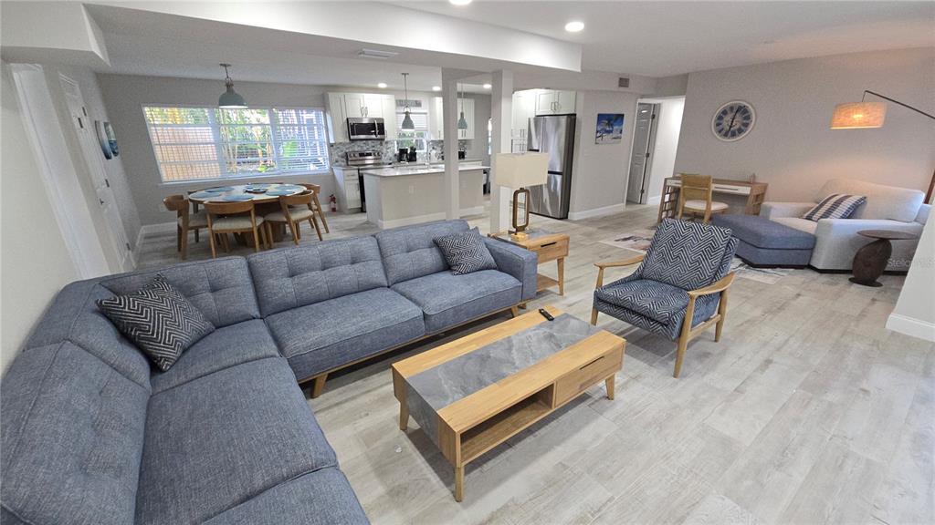 An open-concept living room and kitchen featuring a blue sectional sofa and light wood flooring — 2107 PINE TERRACE, SARASOTA, FL