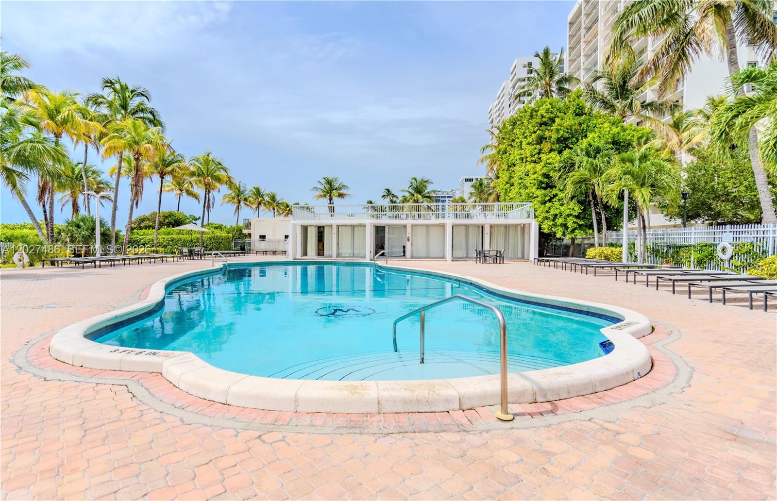 An outdoor swimming pool with a metal handrail is surrounded by a brick patio and palm trees — 2655 Collins Ave # 603, Miami Beach FL 33140, MIAMI BEACH, FL