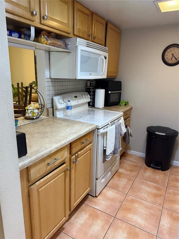 A kitchen features light wood cabinets, a white stove, a microwave, and tiled flooring — 3240 S SEMORAN BOULEVARD UNIT 14, ORLANDO, FL