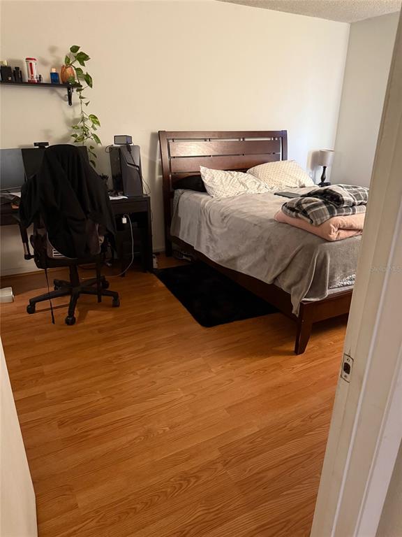 A bedroom features a dark wood bed frame, a desk with a computer, and wood flooring — 3240 S SEMORAN BOULEVARD UNIT 14, ORLANDO, FL