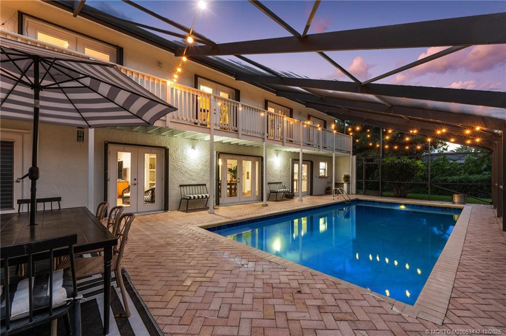 A two-story house exterior features a screened-in pool, brick patio, and string lights at dusk — 4304 SE Fairway E, Stuart FL 34997, STUART, FL
