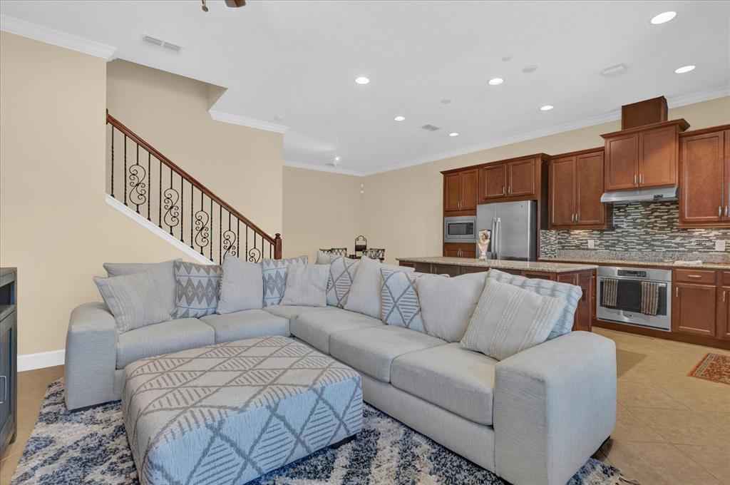 A living room with a large sectional sofa opens into a kitchen with wood cabinets — 9219 LAUREATE BOULEVARD, ORLANDO, FL