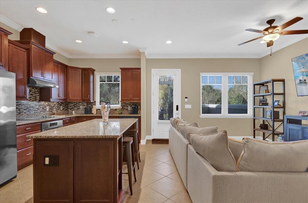 A kitchen with wood cabinets and a granite island opens into a living room area — 9219 LAUREATE BOULEVARD, ORLANDO, FL