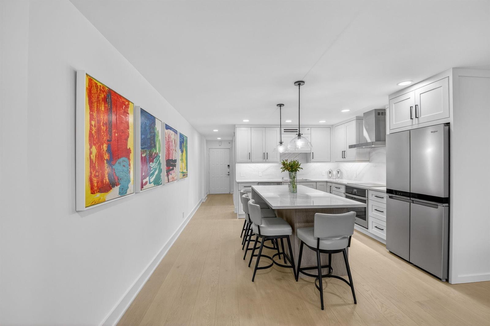 A modern kitchen features white cabinetry, a central island with bar seating, and colorful wall art — 3400 S Ocean Boulevard # 10m, Highland Beach FL 33487, HIGHLAND BEACH, FL