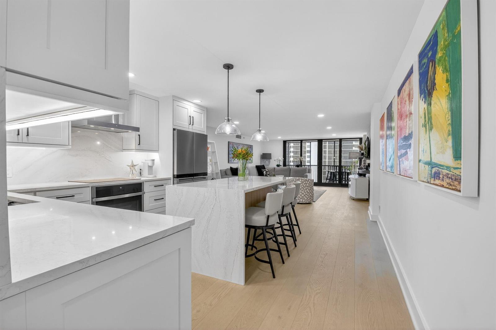 A modern kitchen with white cabinetry, a marble island, and bar seating opens to a living area — 3400 S Ocean Boulevard # 10m, Highland Beach FL 33487, HIGHLAND BEACH, FL