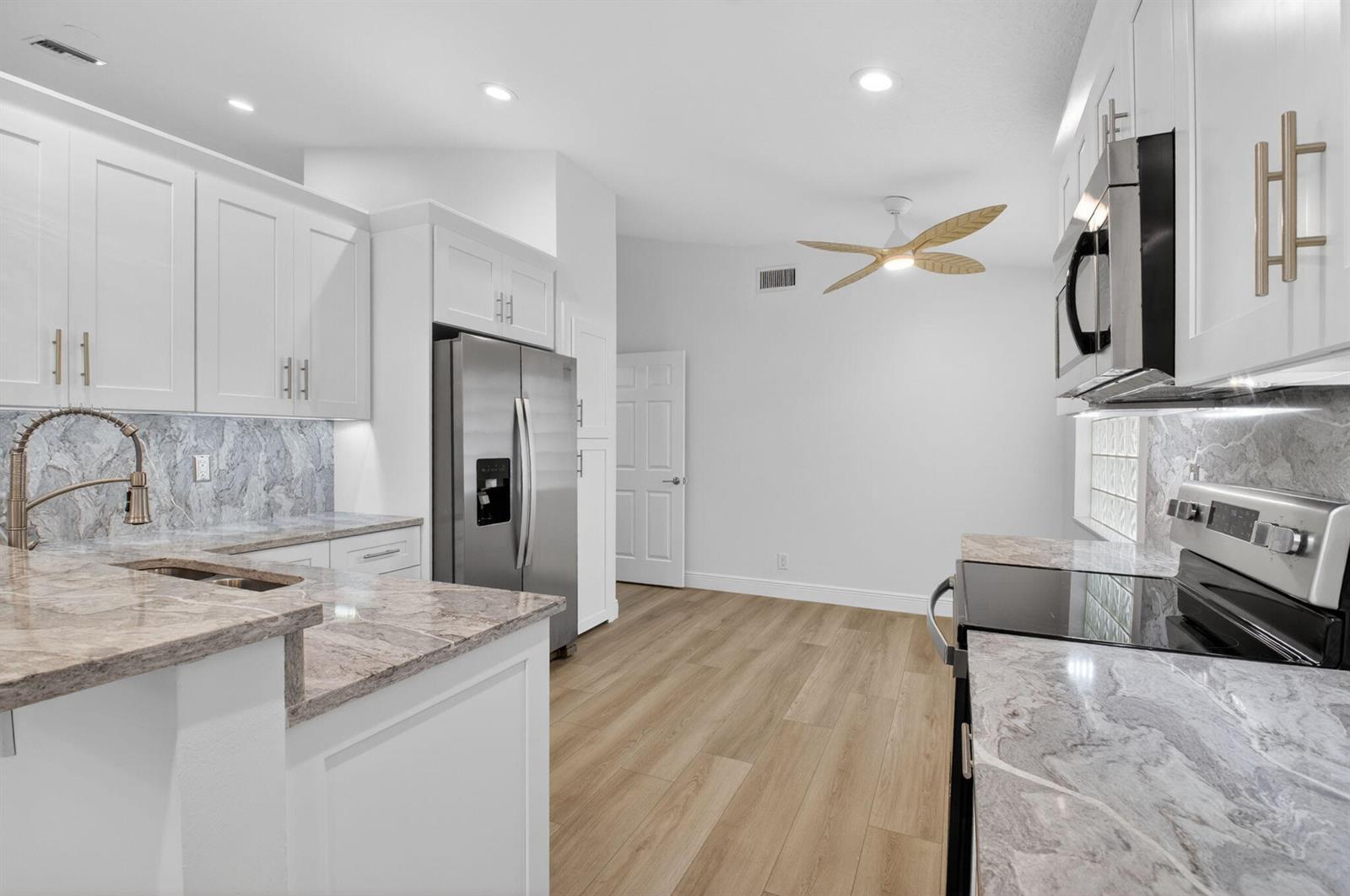A modern kitchen features white cabinets, marble-patterned countertops, stainless steel appliances, and wood-look flooring — 5891 Royal Isles Boulevard, Boynton Beach FL 33437, BOYNTON BEACH, FL