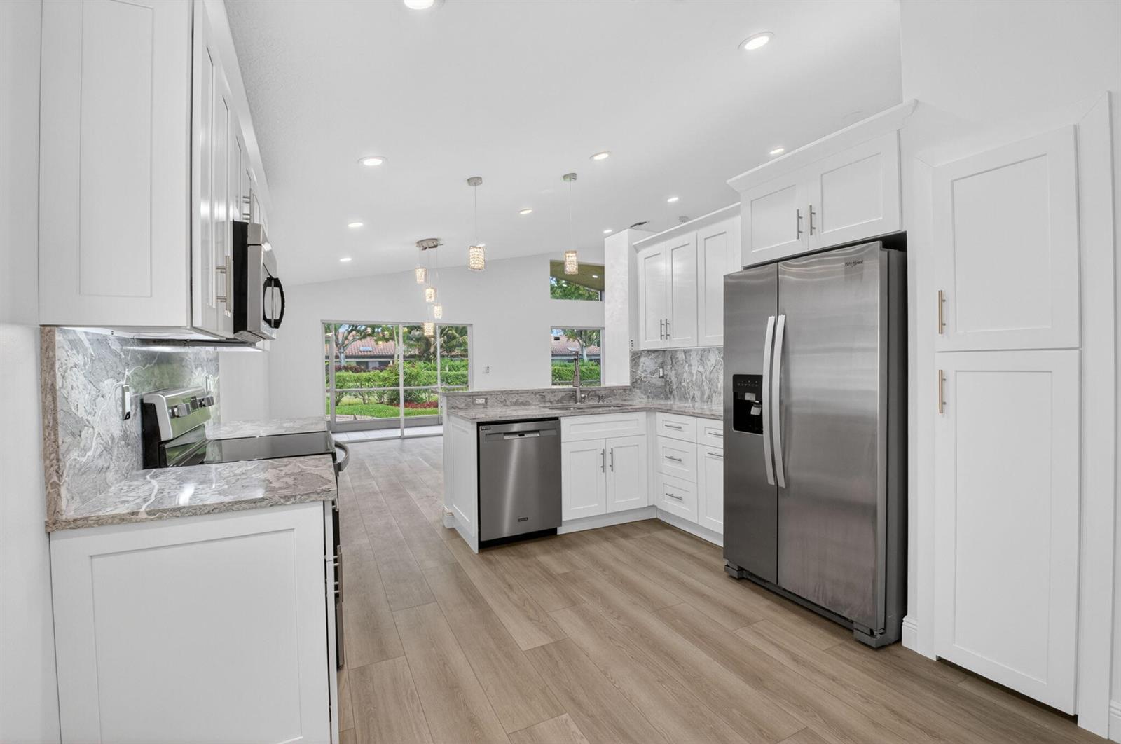 A modern kitchen features white cabinets, stainless steel appliances, marble countertops, and light wood flooring — 5891 Royal Isles Boulevard, Boynton Beach FL 33437, BOYNTON BEACH, FL