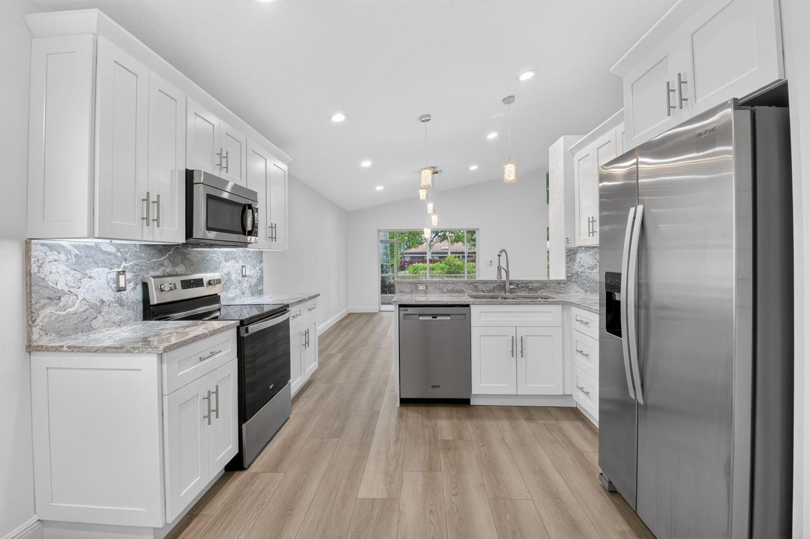 A modern kitchen features white cabinets, stainless steel appliances, marble-patterned countertops, and light wood flooring — 5891 Royal Isles Boulevard, Boynton Beach FL 33437, BOYNTON BEACH, FL