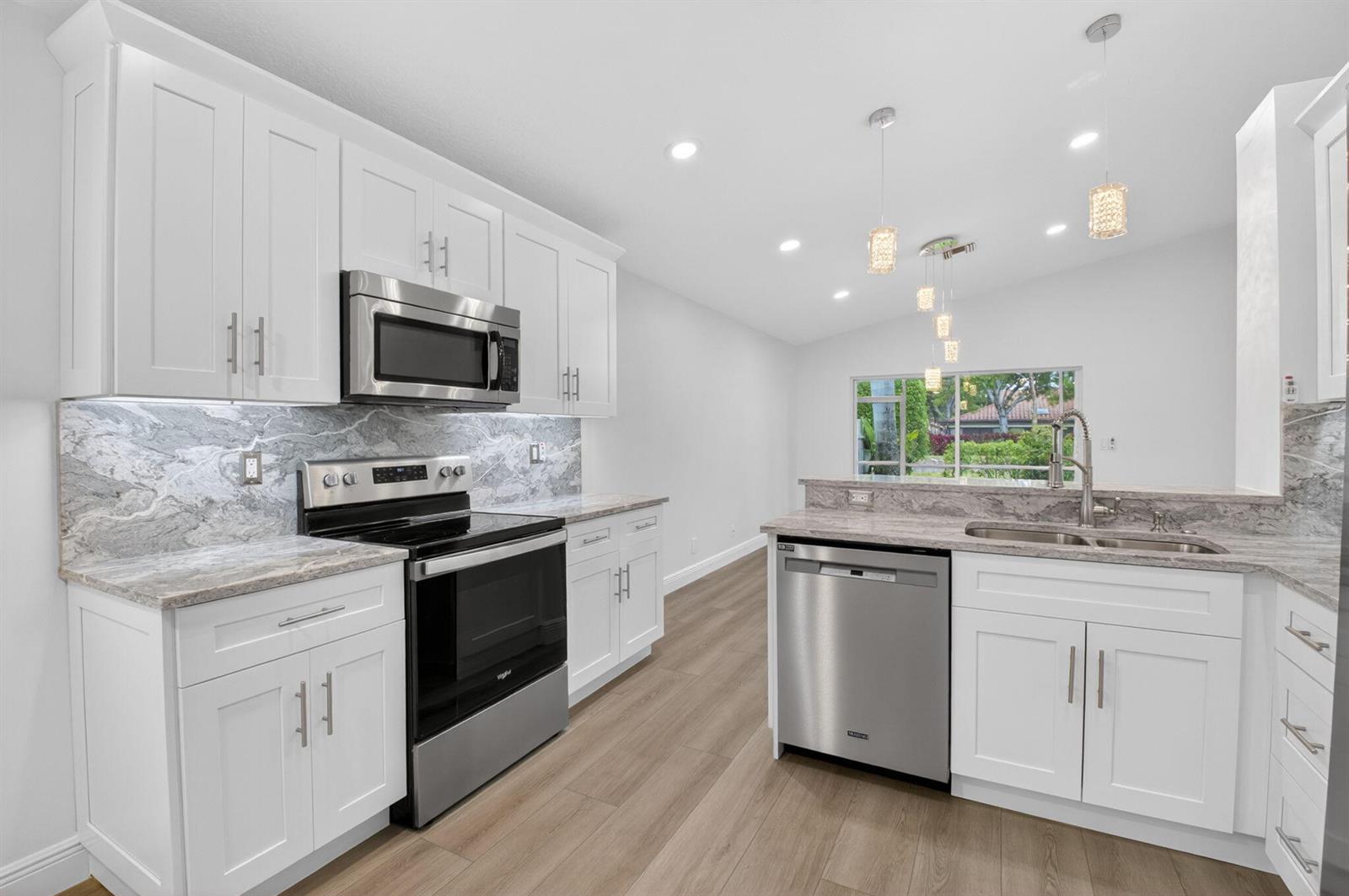 A modern kitchen features white cabinets, stainless steel appliances, and gray marble-patterned countertops and backsplash — 5891 Royal Isles Boulevard, Boynton Beach FL 33437, BOYNTON BEACH, FL