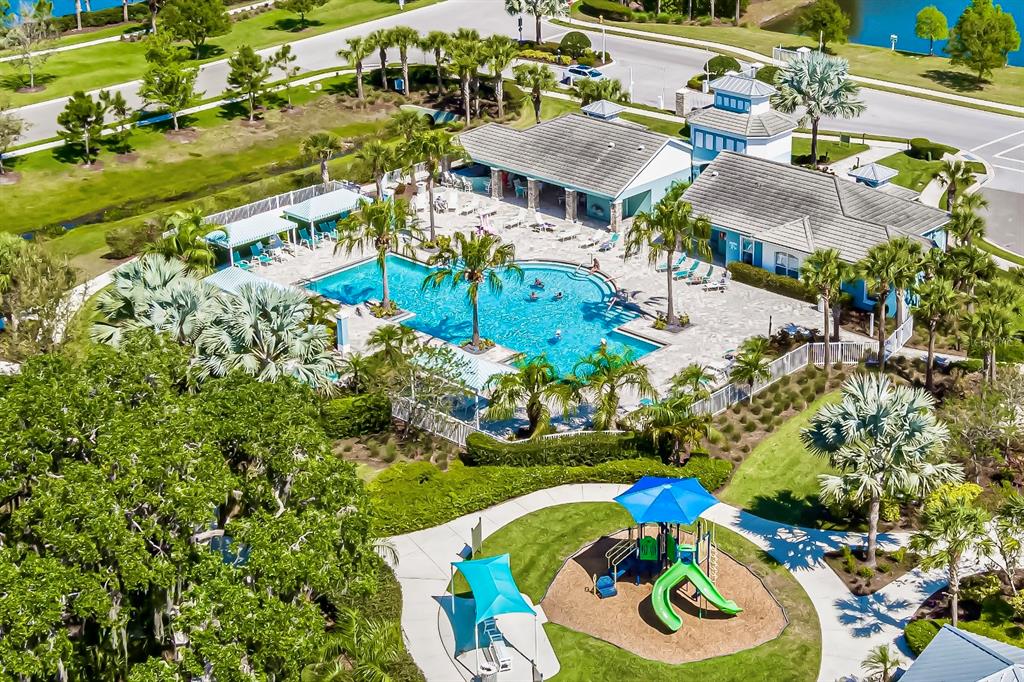An aerial view of a community swimming pool, clubhouse, and playground surrounded by lush landscaping — 4028 WILDGRASS PLACE, PARRISH, FL