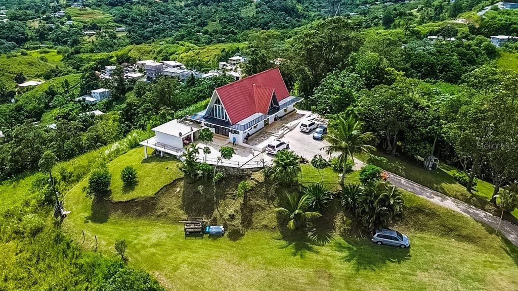 An aerial view shows a house with a red roof situated on a grassy hill — PR 152 PR 773, BARRANQUITAS, PR
