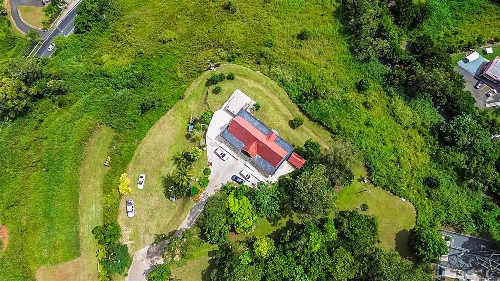 An aerial view shows a building with a red roof surrounded by green grassy hills — PR 152 PR 773, BARRANQUITAS, PR