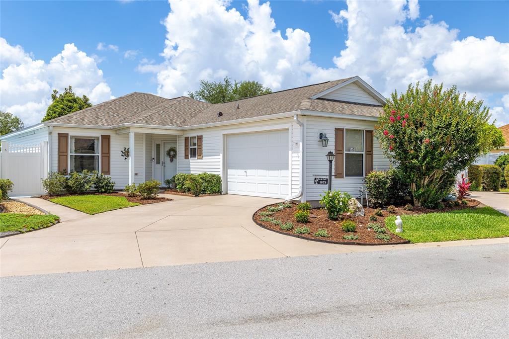 A single-story white house with a garage, driveway, and landscaped front yard under a blue sky — 1678 GOVAN PLACE, THE VILLAGES, FL