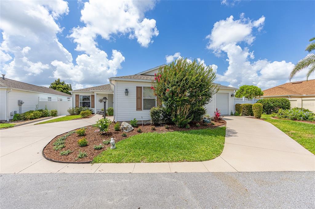 A single-story white house with a curved driveway, landscaped front yard, and a large bush — 1678 GOVAN PLACE, THE VILLAGES, FL