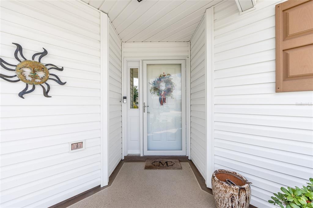 A front entryway features white horizontal siding, a glass storm door, and a sun wall decoration — 1678 GOVAN PLACE, THE VILLAGES, FL