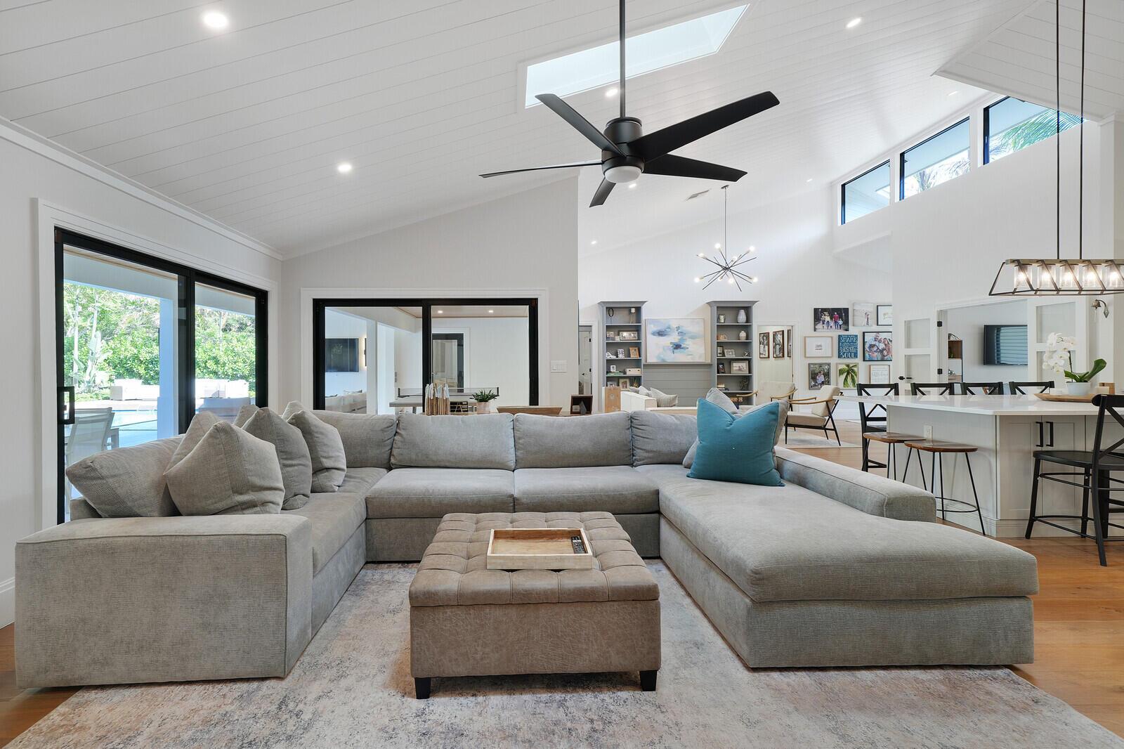 A spacious living room features a large grey sectional, tufted ottoman, and vaulted ceilings — 19526 W Trails End Terrace, Jupiter FL 33458, JUPITER, FL