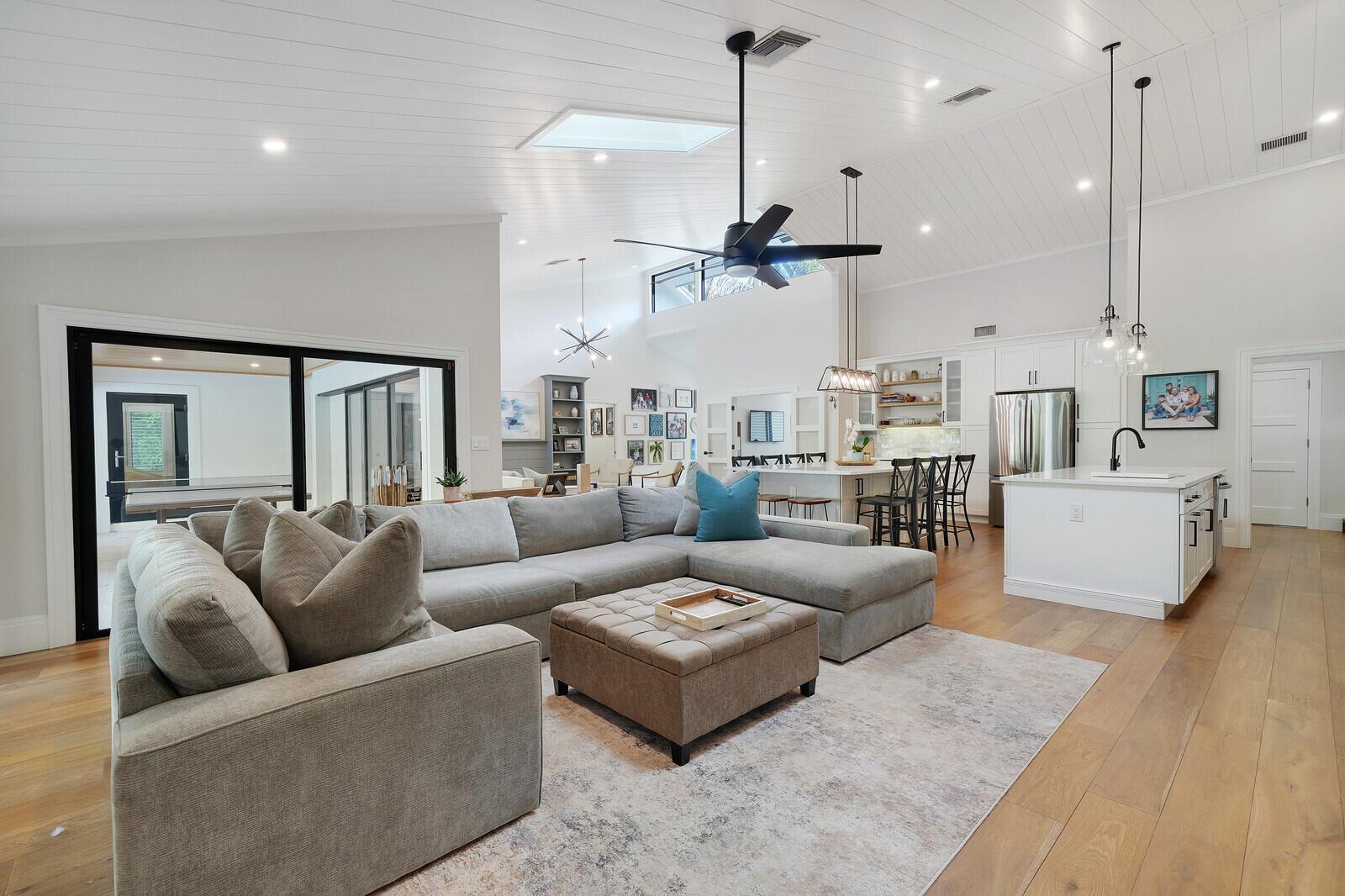 A spacious open-concept living room and kitchen featuring vaulted ceilings, hardwood floors, and neutral furniture — 19526 W Trails End Terrace, Jupiter FL 33458, JUPITER, FL