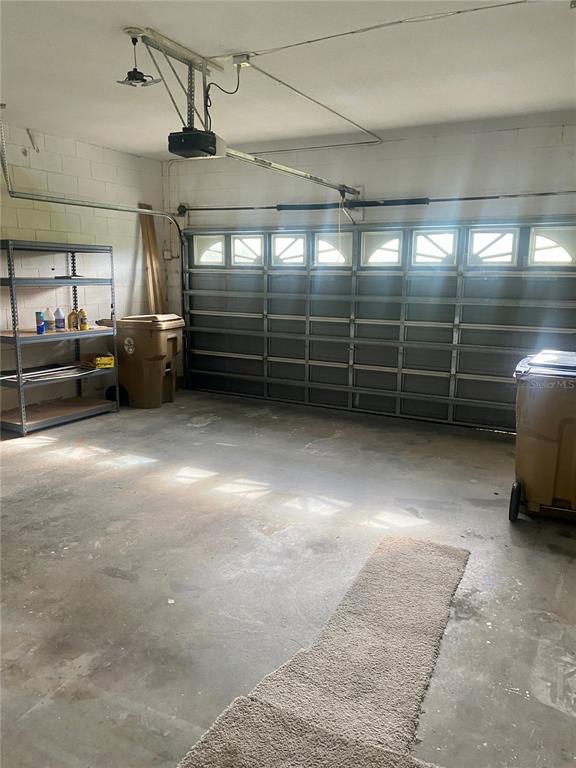 A garage with a concrete floor, metal shelving, and a sectional overhead door — 1690 BIG OAK LANE, KISSIMMEE, FL