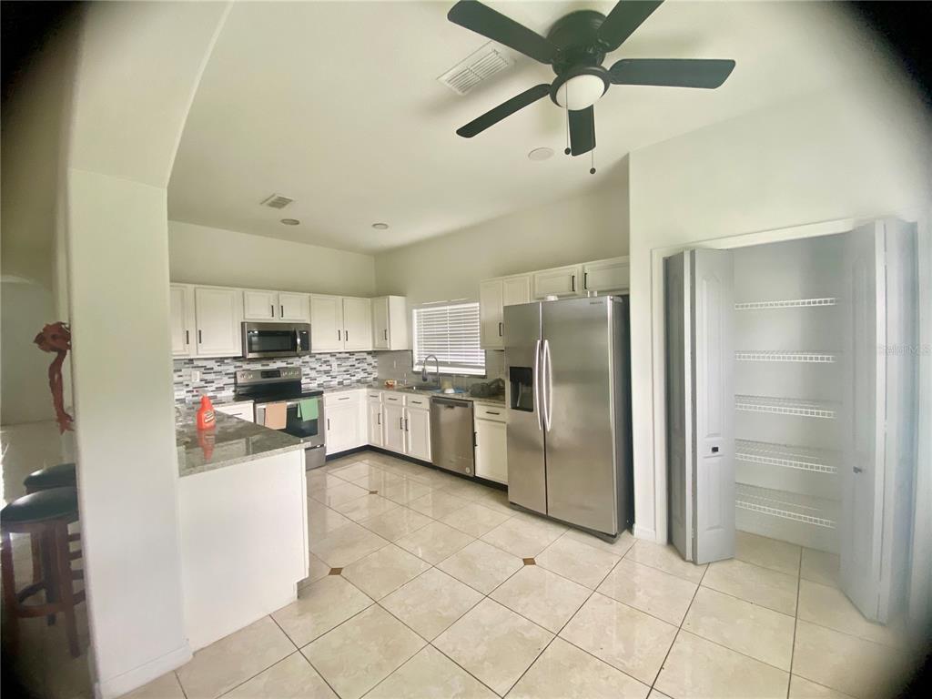 A kitchen features white cabinets, stainless steel appliances, granite countertops, and a walk-in pantry — 1690 BIG OAK LANE, KISSIMMEE, FL