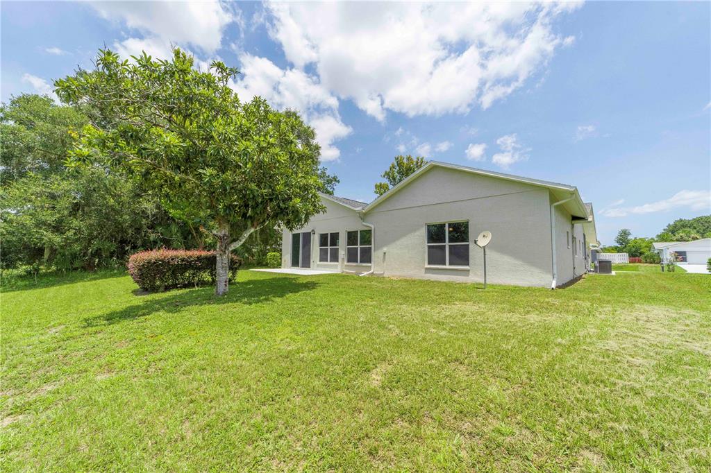 The exterior of a light-colored house features a large grassy yard and a mature tree — 10 BLYTH PLACE, PALM COAST, FL
