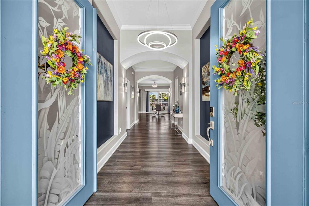 A view through double blue glass-paneled doors into a long hallway with dark wood flooring — 4251 TENNYSON WAY, VENICE, FL