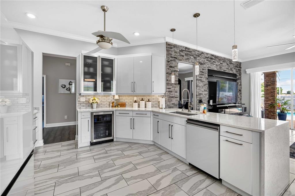 A modern kitchen features white cabinetry, stone-tiled backsplash, a stone accent wall, and tiled flooring — 4251 TENNYSON WAY, VENICE, FL